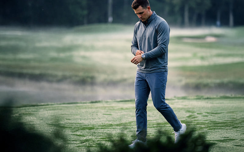 A man in a performance gray long-sleeve quarter-zip pullover and matching gray pants walking on a misty golf course.